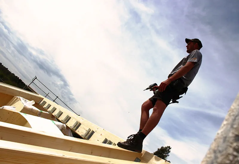 Ein Zimmermann mit dem Akku-Bohrschrauber DRC 18/4 von Festool auf dem Dach eines Massivholzhauses.