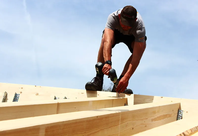 Ein Zimmermann mit dem Akku-Bohrschrauber DRC 18/4 von Festool auf dem Dach eines Massivholzhauses.