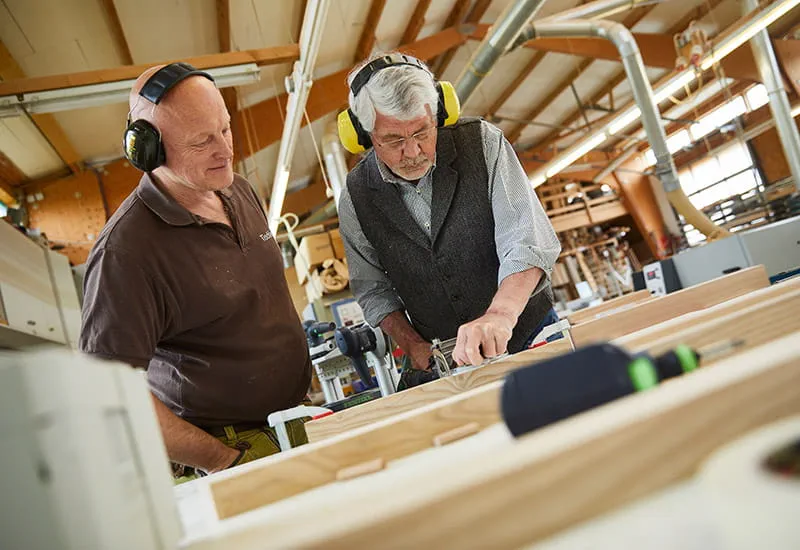Der Tischler Schillings und sein Kunde Möllmann betrachten die Strukturen des Holzes.