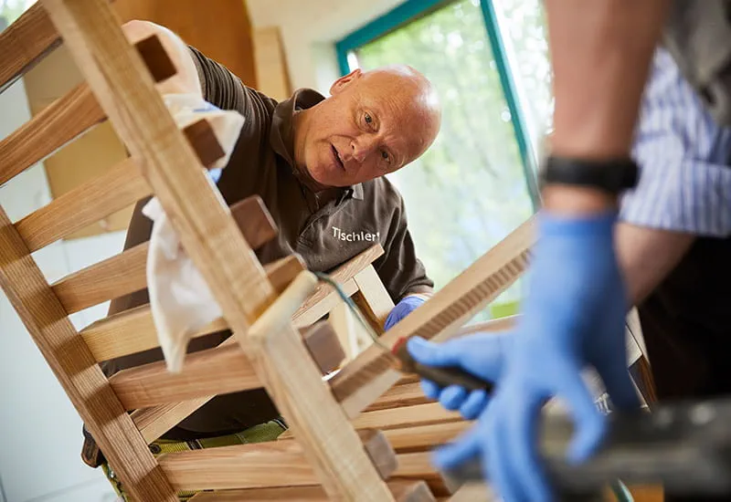 Tischler Schillings ölt die Oberflächen des Schaukelstuhls.