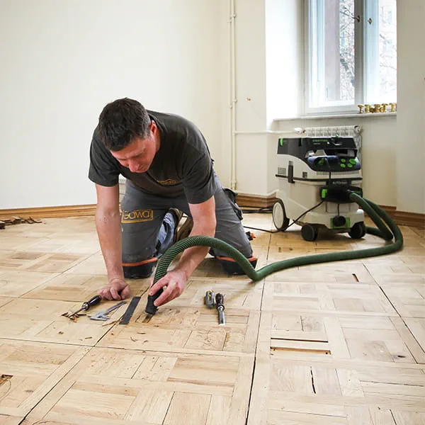Parkettlegermeister Jarek Gawina löst defekte Teile aus dem  Parkettboden und  entfernt sie mit dem Festool Absaugmobil