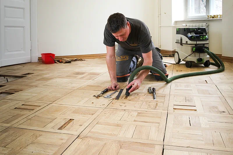 Parkettlegermeister Jarek Gawina löst defekte Teile aus dem Parkettboden und entfernt sie mit dem Festool Absaugmobil