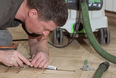 Mit Präzision und Geduld entfernt Jarek tief über das Parkett gebeugt Unebenheiten mit dem Stechbeitel